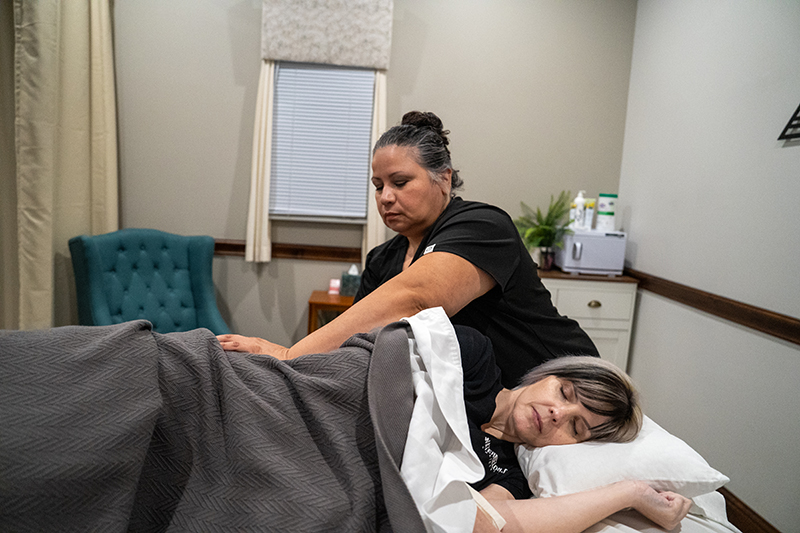 A woman receives a massage at Frisco Massage Therapy while lying on her side in a treatment room, covered with a gray blanket, as a therapist works on her back to help alleviate prenatal discomfort.