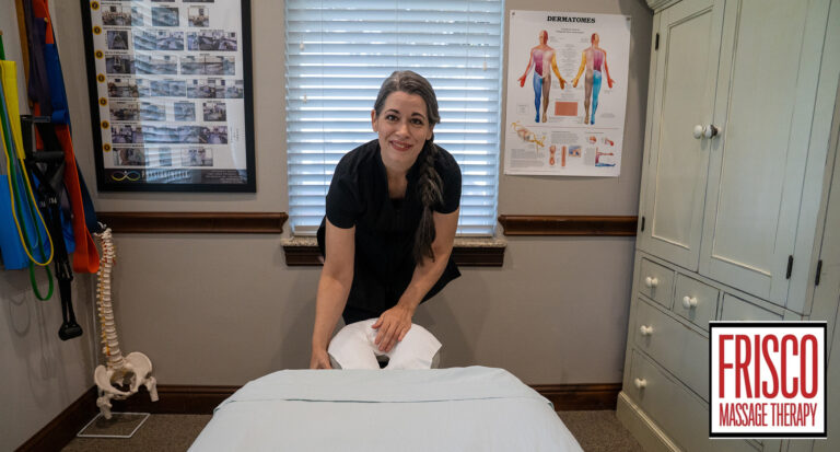 A woman prepares a massage table in a therapy room with anatomical charts, exercise bands, and a spine model, highlighting the "Frisco Massage Therapy" logo—perfect for those seeking therapeutic massage Frisco services.