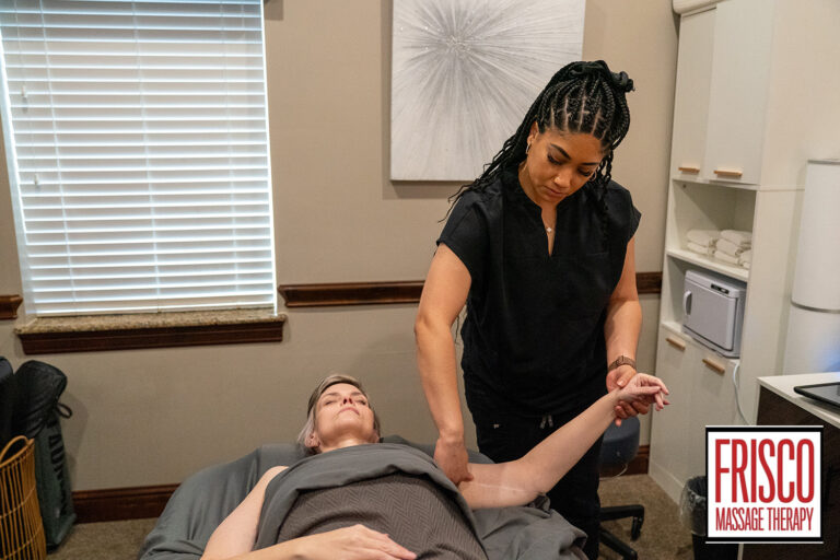 A massage therapist, skilled in lymphatic drainage specialists’ techniques, stretches a client's arm in a tranquil treatment room at Frisco Massage Therapy.