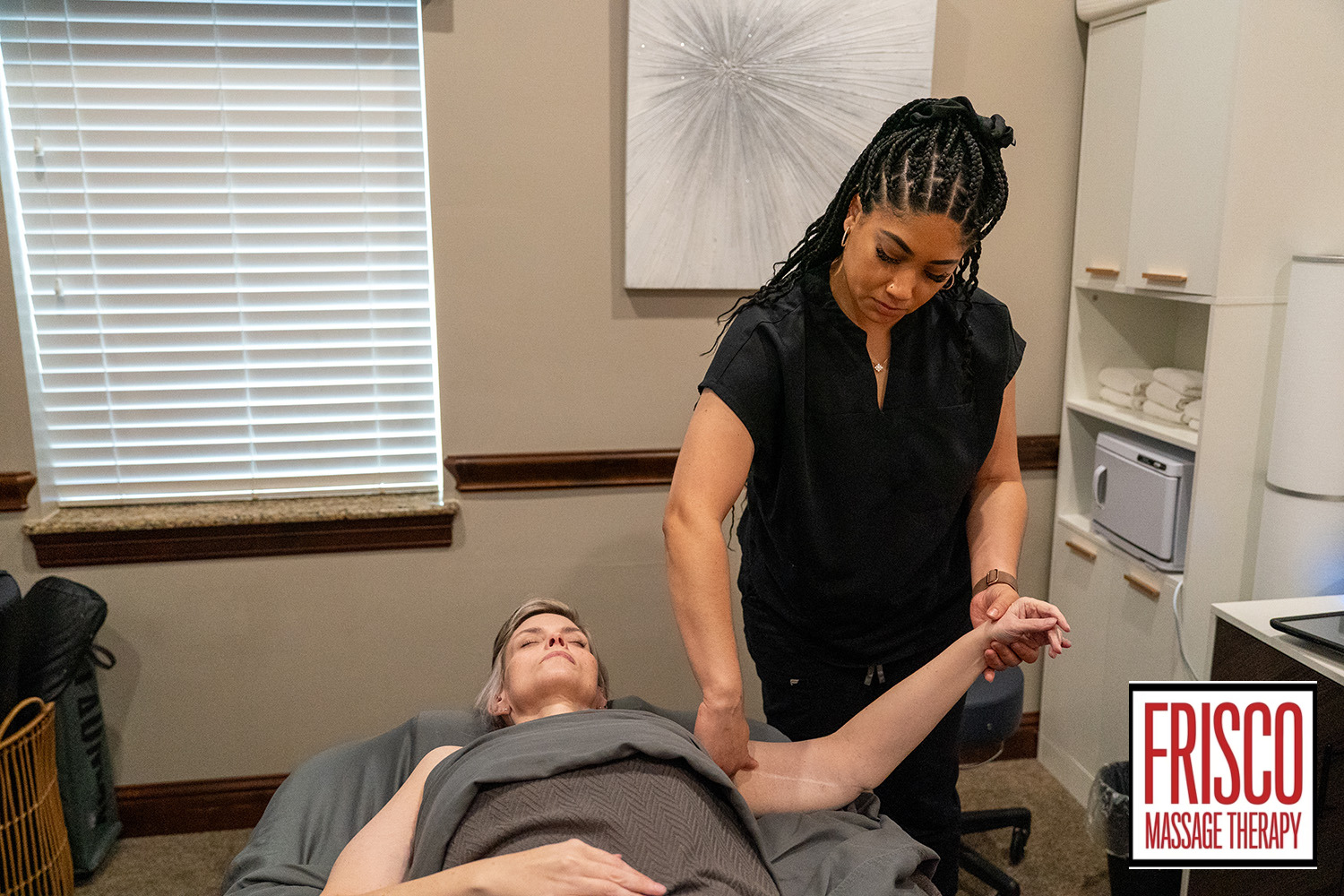 A massage therapist, skilled in lymphatic drainage specialists’ techniques, stretches a client's arm in a tranquil treatment room at Frisco Massage Therapy.