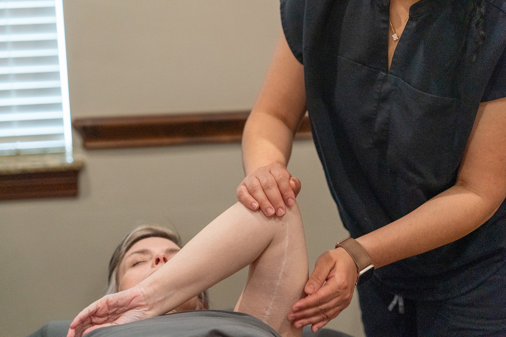 A person lies on a table while another supports and stretches their arm at the elbow during a Scar Tissue Therapy session, providing targeted treatment—ideal for those seeking scar tissue therapy in Frisco TX.