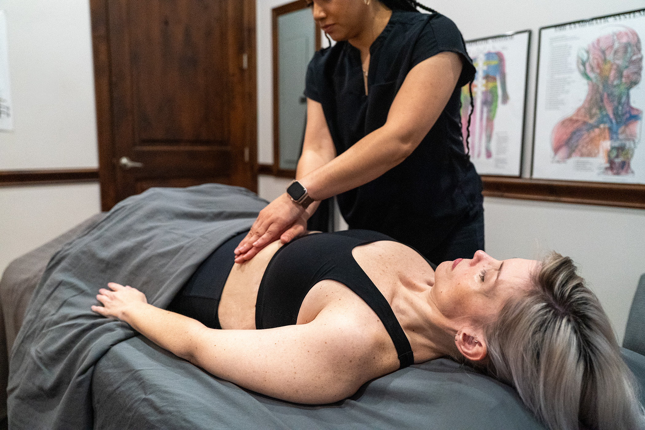 A massage therapist uses both hands to apply pressure to a client’s abdomen during Scar Tissue Therapy as the client lies on a table in a treatment room.