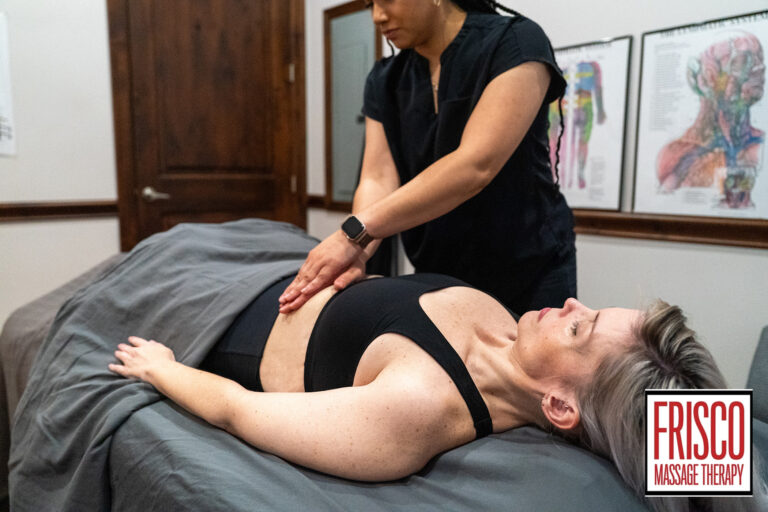 A massage therapist performs abdominal massage for scar pain on a woman lying on a table in a clinic room. The "Frisco Massage Therapy" logo is visible in the lower right corner.