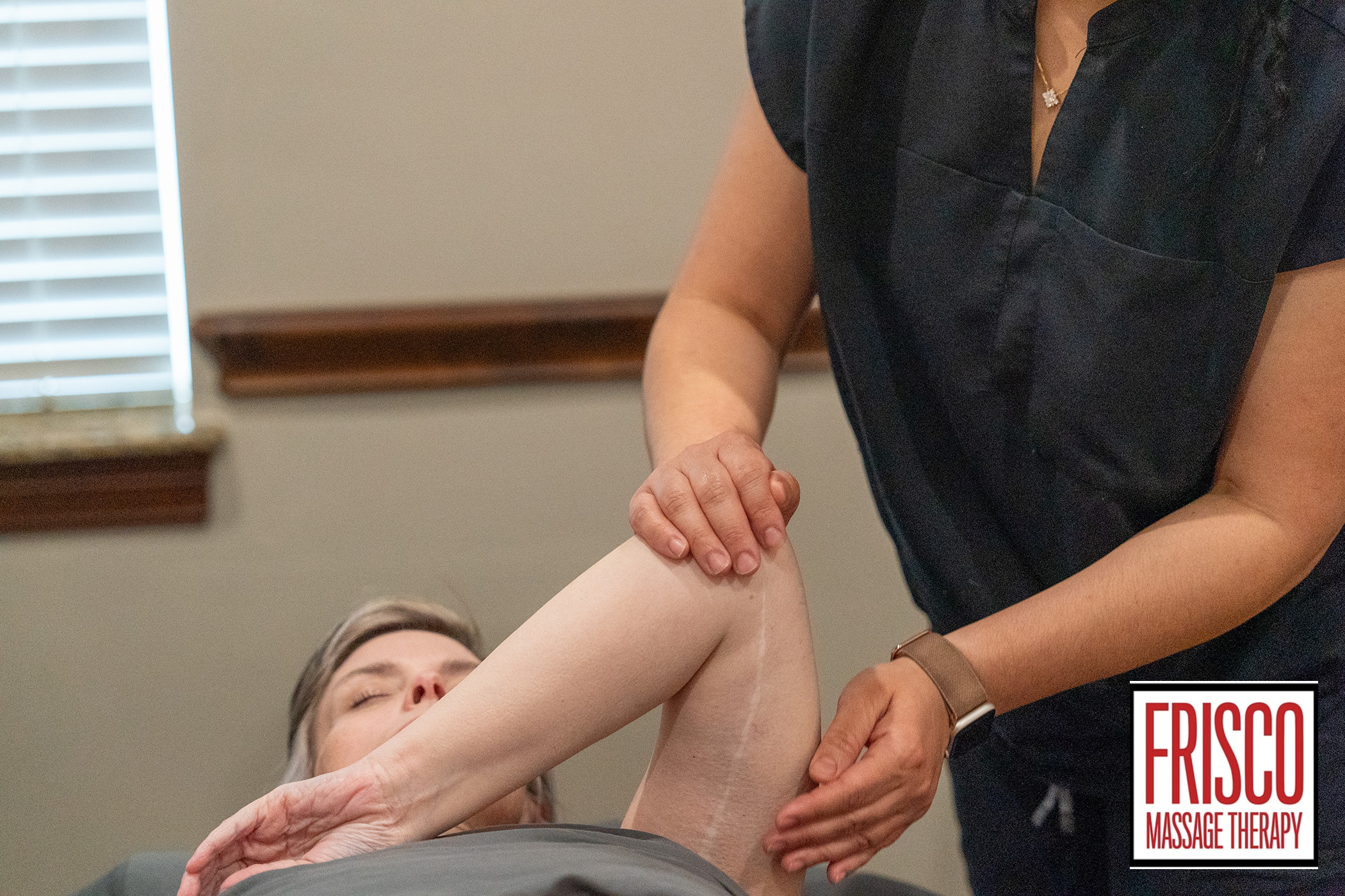 A massage therapist stretches a client's arm while the client lies on a table at Frisco Massage Therapy, offering specialized massage therapy for scar pain.