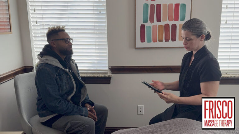 A man sits on a chair while a woman in uniform reviews a clipboard, discussing sports massage for injury prevention; blinds and artwork are visible in the background. Frisco Massage Therapy logo is in the lower right corner.