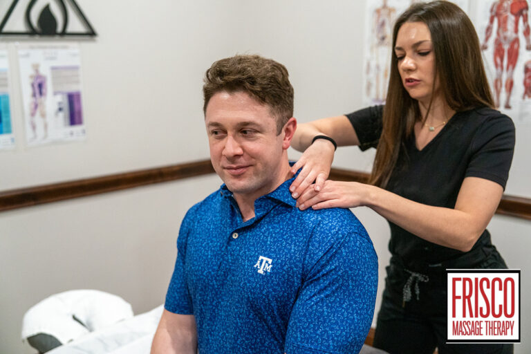A woman in black scrubs massages the shoulders of a man wearing a blue Texas A&M shirt in a clinic room. The logo "Frisco Massage Therapy" is visible in the corner, highlighting their expertise in massage and cupping techniques.