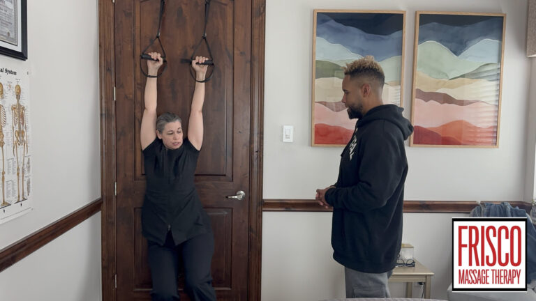 A person hangs from straps attached to a door while another observes in a room with anatomical charts, framed artwork, and hints of cupping therapy. The "Frisco Massage Therapy" logo is visible.