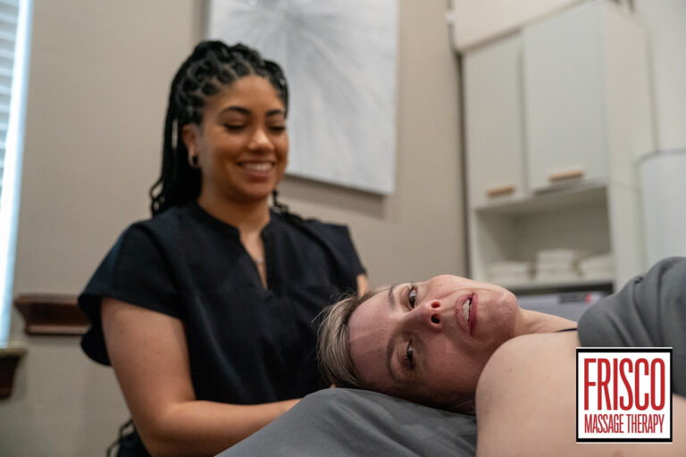 A massage therapist stands beside a client lying on a massage table at Frisco Massage Therapy, providing post-operative lymphatic drainage care. The client looks relaxed, and the therapist is smiling.