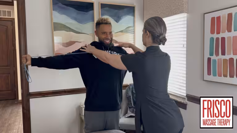 A massage therapist assists a man with an arm mobility exercise in a well-lit room, demonstrating the benefits of sports massage for injury prevention. The Frisco Massage Therapy logo is visible in the bottom right corner.